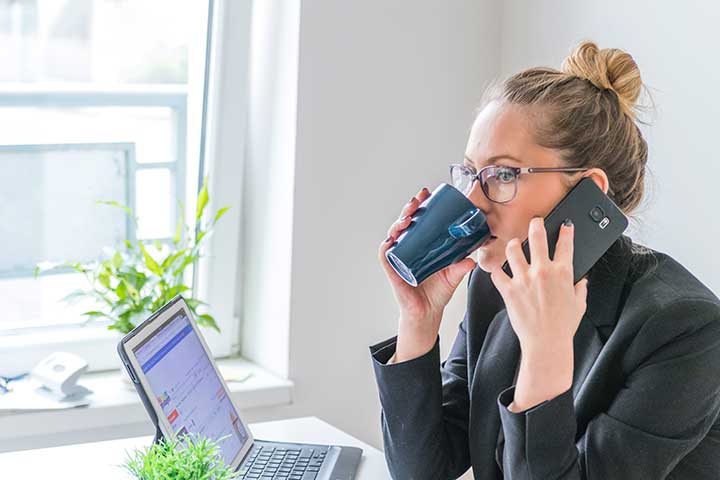 person pratar i telefon och dricker kaffe framför en laptop